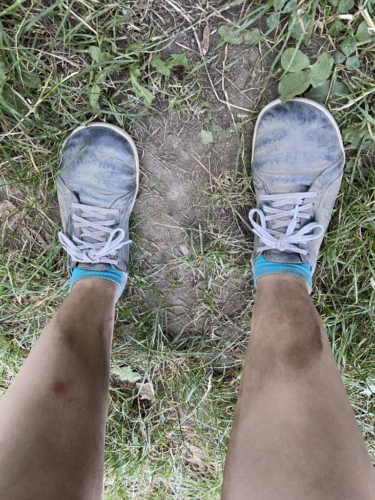 Blick hinunter auf schmutzige Beine und ehedem schwarze, schmutzige Schuhe.