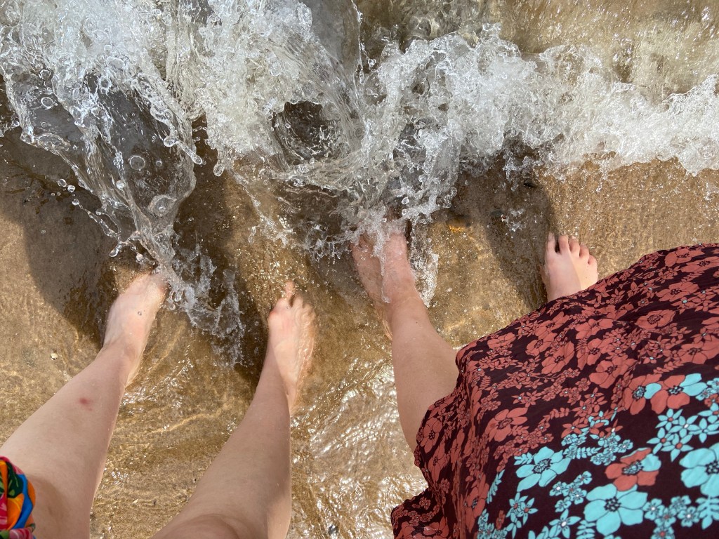 Zwei Paar Füße am sandigen Rheinufer im Wasser  