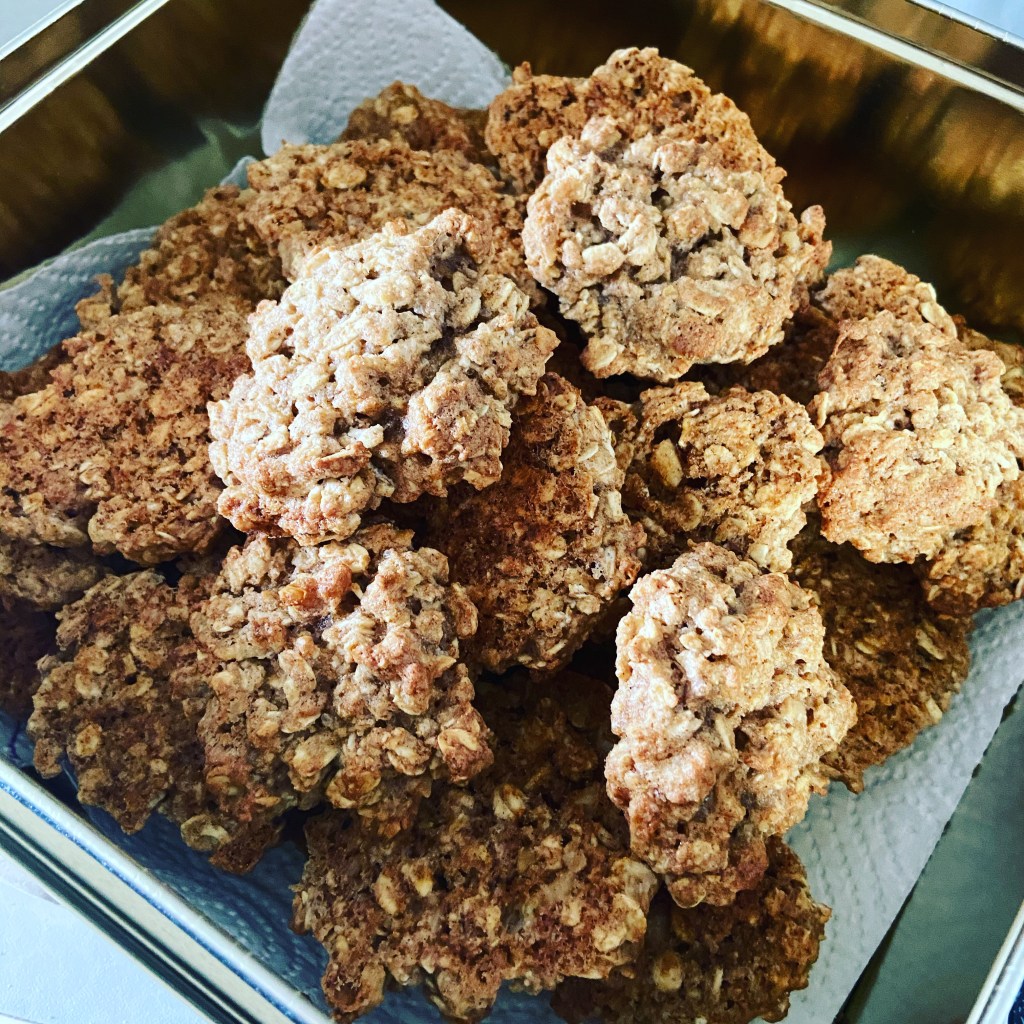 Großaufnahme einer Keksdose aus Metall, ausgelegt mit einem Stück Küchenrolle. Darauf ein Berg Haferflockenkekse.