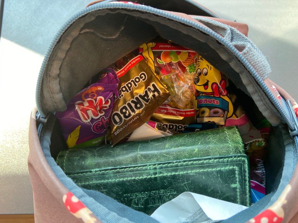 Ein geöffneter Rucksack, darin erkennt man ein grünes Portemonnaie und diverse Tüten mit Haribo-Süßigkeiten.