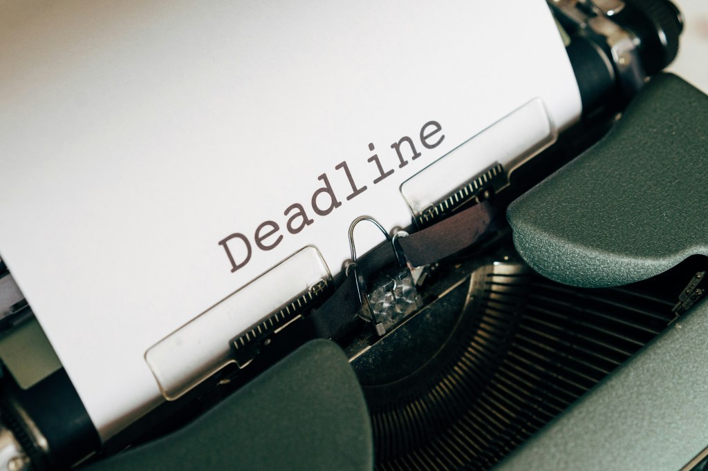 Ein weißes Blatt ist in eine altmodische Schreibmaschine eingespannt. Nahaufnahme. Große Schrift: "Deadline".