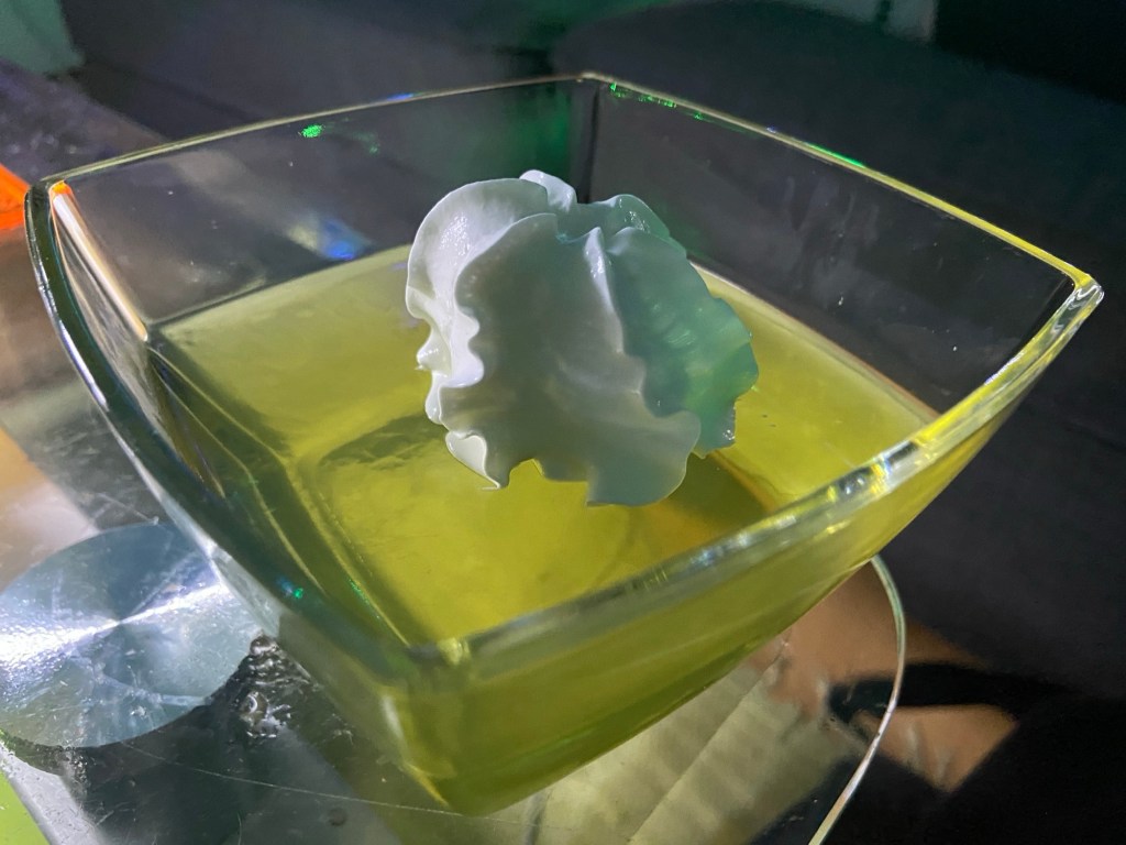 Großaufnahme: Zitronengötterspeise mit Sahne-Tuft in einer eckigen Glasschale.