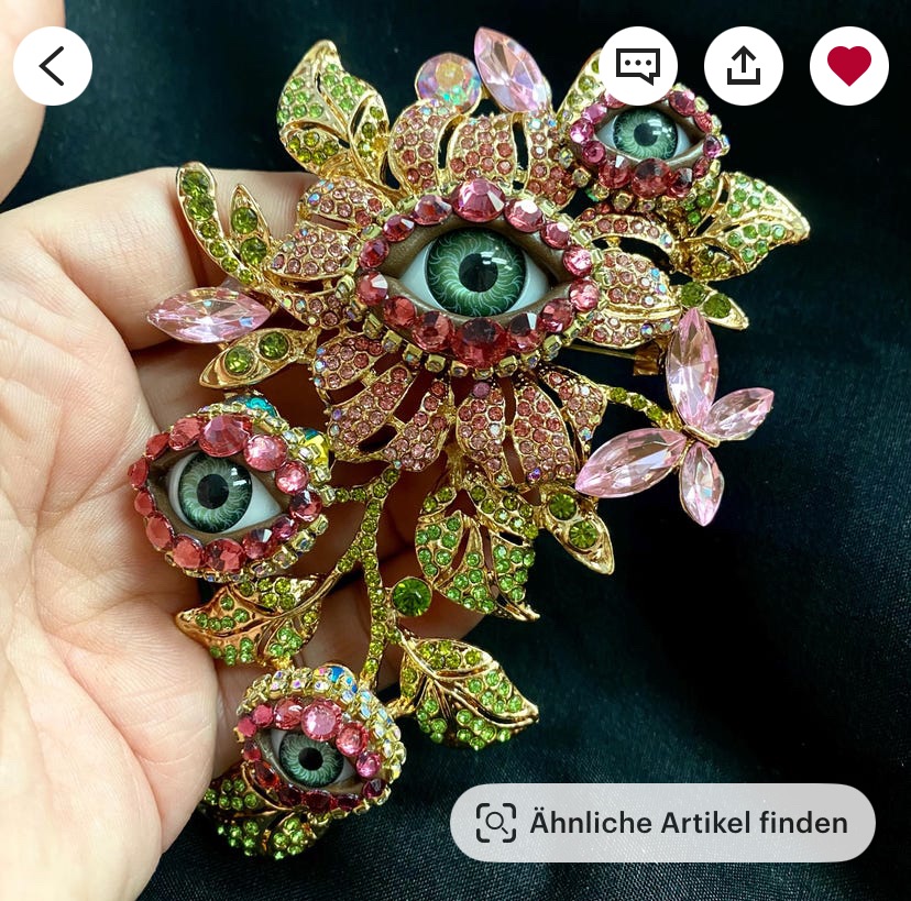 Eine Brosche aus menschlichen Augen, die aus einer Pflanzenranke hervorschauen.