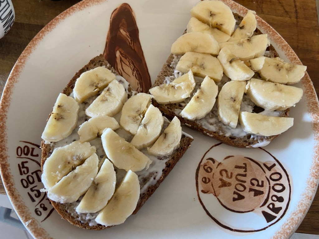 Auf einem Teller liegen zwei halbe Scheiben Körnerbrot, darauf Mayonnaise und halbierte Bananenscheiben.