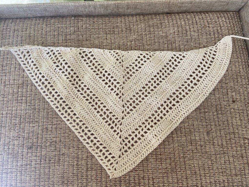 Eine naturweiße Häkel-Bandana, flach ausgebreitet. Das Muster ist regelmäßig und besteht aus soliden Streifen und luftigen Kästchen.