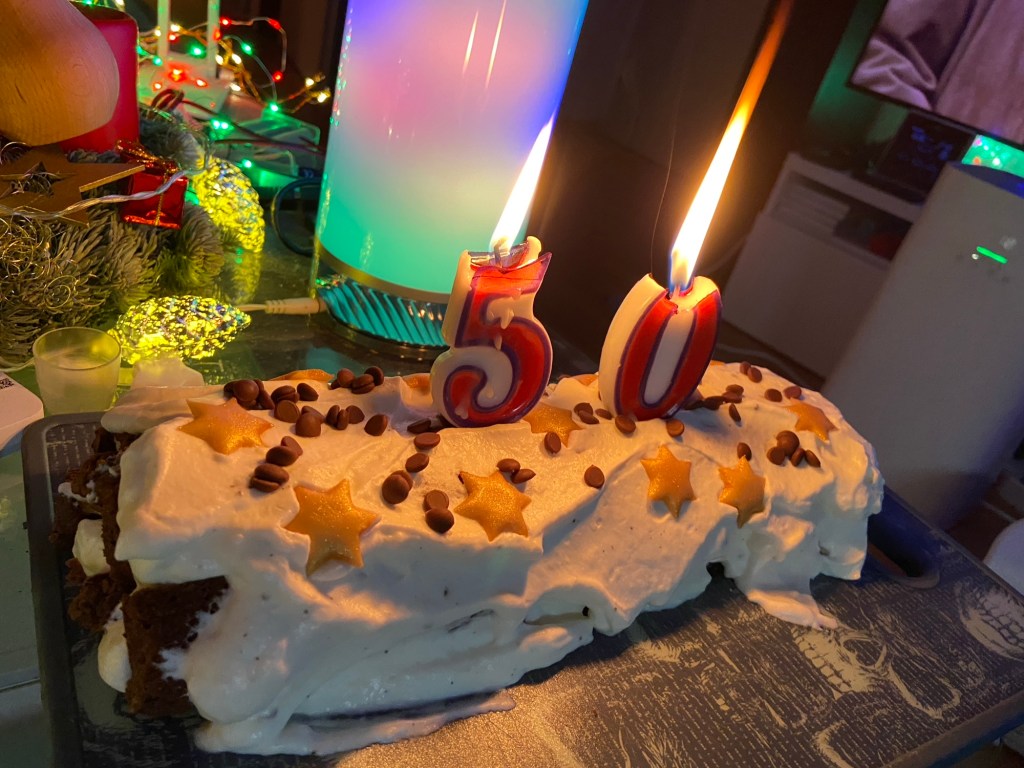 Eine mit Sahne bestrichene Kuchenrolle, dekoriert mit Schokotropfen, goldenen Marzipansternen und einer brennenden 50. 