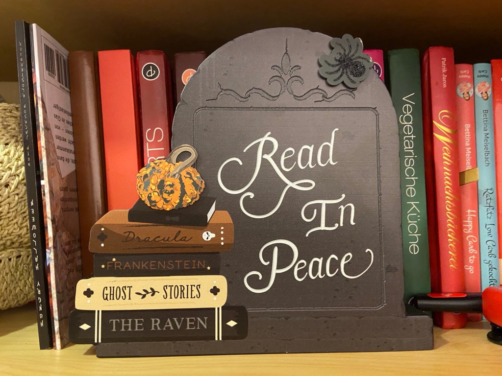 Vor einer Reihe Kochbücher steht ein Grabstein aus Holz, auf den "Read in Peace" geschrieben steht. 